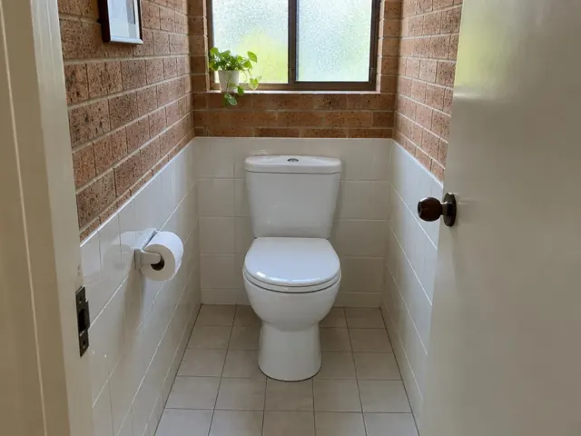 Clean white toilet in a tiled small bathroom with brick walls and a frosted window in Box Hill